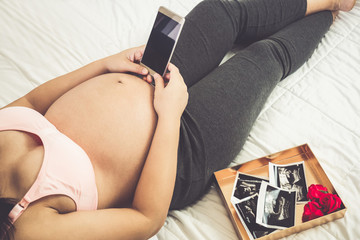 Pregnant woman feeling happy at home while taking care of her child. The young expecting mother...