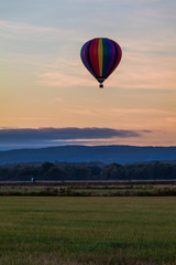 Naklejka premium Rainbow hot-air balloon floats over field at sunrise, portrait
