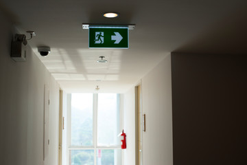 Fototapeta na wymiar Sign : Emergency exit sign at path way indoor building public facility that emergency escape route is left. (fire, building, health or safety) require exit signs to be permanently lit