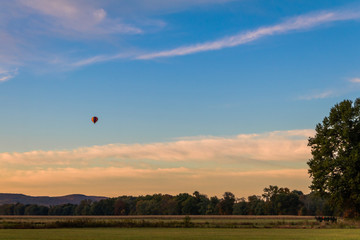Rainbow hot-air balloon floats over field at sunrise