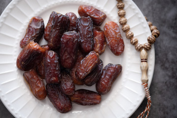 Dates, rosary on white ceramic plate. Ramadan concept.
