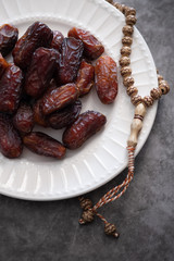 Dates, rosary on white ceramic plate. Ramadan concept.