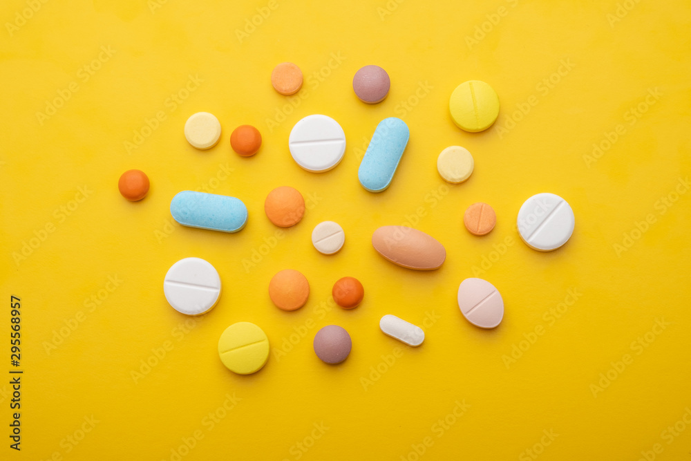 Wall mural top view colorful medical pills on yellow background.