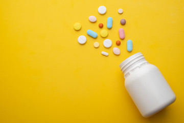Top view colorful medical pills and white bottle on yellow background