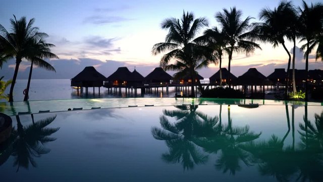 Luxury hotel vacation travel destination - beach, palm trees overwater bunglow resort and luxury infinity swimming pool at amazing tropical night