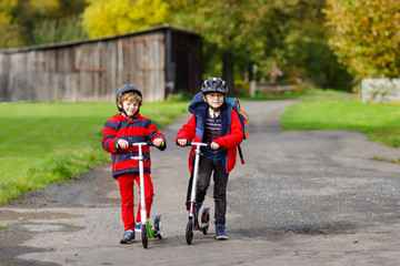 Fototapeta premium Two little kids boys riding on push scooters on the way to or from school. Schoolboys of 7 years driving through rain puddle. Funny siblings and best friends playing together. Children school out.