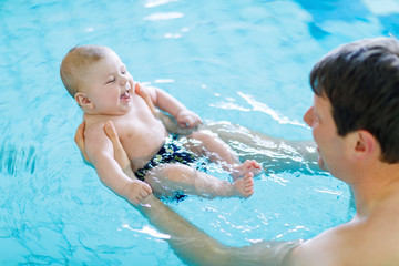 Happy middle-aged father swimming with cute adorable baby in swimming pool.