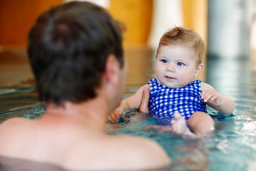 Obraz premium Happy middle-aged father swimming with cute adorable baby girl in swimming pool.