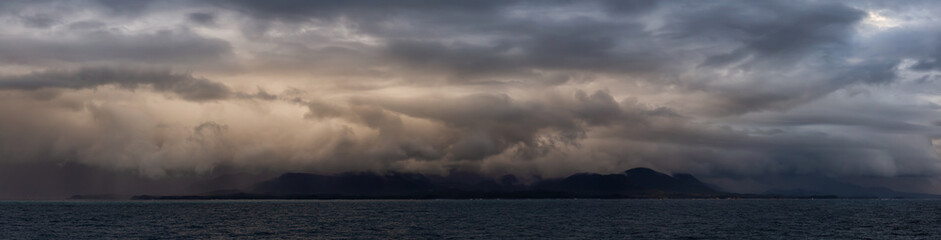Dramatic Panoramic View of a cloudscape during a dark, rainy and colorful sunset. Taken on the Ocean Coast of Alaska, USA.