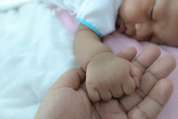 The baby's hand holding his father's finger while sleeping on the soft gentle bed, sufficient sleep is brain food. Allowing the body to rest Good mood, fresh and clear Create immunity