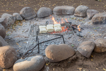 Traditional South African braai broodjies toasted sandwiches are prepared outdoors over an open...