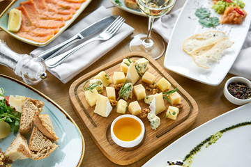 Cheese plate. Focus on delicious cheese mix with walnuts, honey on wooden table. Various snacks and antipasti on the table. Restaurant menu.