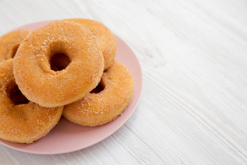 Homemade autumn apple donuts on a pink plate on a white wooden surface, low angle view. Copy space.