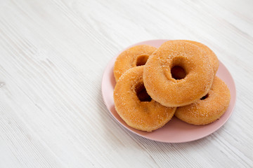 Homemade autumn apple donuts on a pink plate on a white wooden surface, side view. Copy space.
