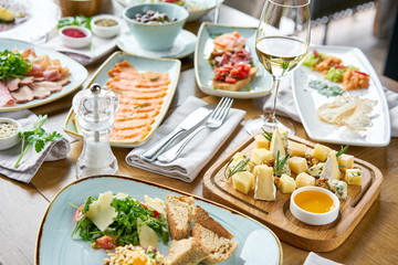 Various snacks and antipasti on the table. Restaurant menu. Cheese plate. Focus on delicious cheese mix with walnuts, honey on wooden table.