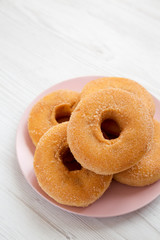 Homemade autumn apple donuts on a pink plate on a white wooden background, low angle view. Copy space.