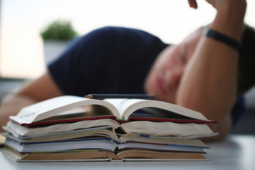 Tired male student at workplace in room taking nap on pile of textbooks. Sleepy man resting during education after sleepless night. Student in despair caused by exam deadline concept