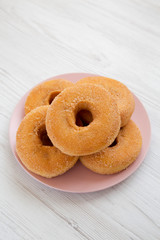 Homemade autumn apple donuts on a pink plate on a white wooden surface, low angle view. Close-up.