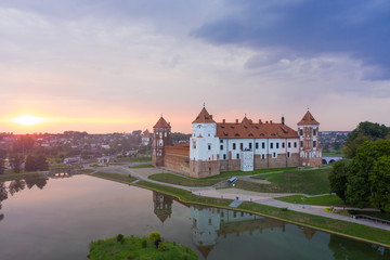 Mirsky Castle and its reflection in the lake in summer. Sunset in cloudy weather with rain clouds.