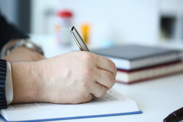 Hand of businessman in suit filling and signing with silver pen partnership agreement form clipped to pad closeup. Management training course some important document team leader ambition concept