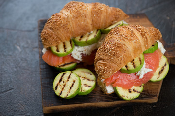 Croissants with red fish, ricotta cheese and grilled zucchini slices, studio shot on a dark brown stone background