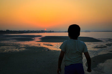 Boy standing and watching the sunset near the seashore
