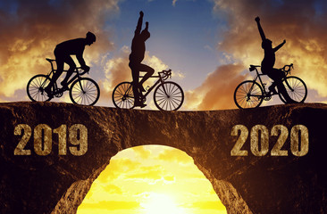 Three cyclists ride a road bicycle at sunset. Forward to the New Year 2020.