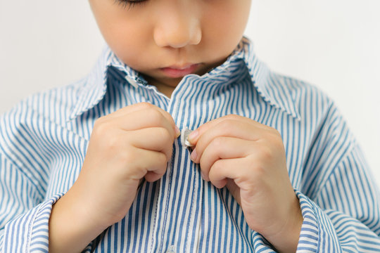 Child Development concept: Close up of a little kindergarten boy's hands learning to get dressed, buttoning his striped blue shirt. Montessori practical life skills - Care of self, Early Education.