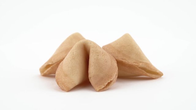 Close-up circling around shot of three crispy fortune cookies spinning slowly on the table. Isolated, on white background.
