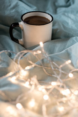 Coffee cup and garland on a bed. Atmospheric hygge style. Cozy winter or autumn concept