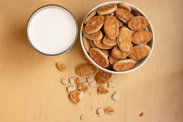 Fat cookies in a bowl, glass cup with milk, light brown wooden background.