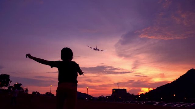 Silhouette kids playing aeroplane toy in sunset,slow-motion