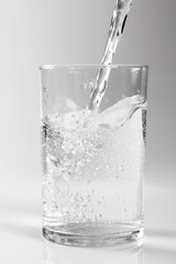 Pouring clear water into glass. Isolated on white background.