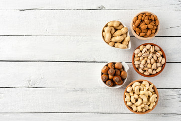 Nuts: almonds, pistachios, peanuts, hazelnuts and cashews in bowls on white wooden background with copyspace