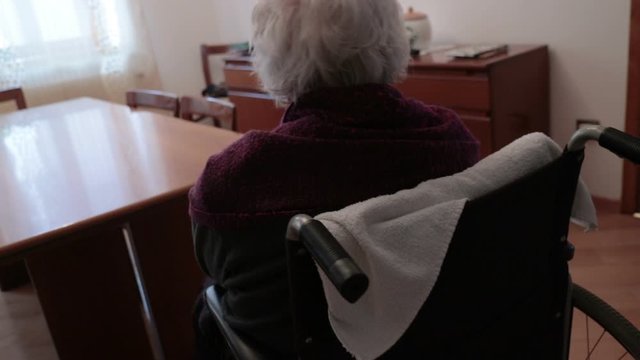 Lonely old woman at home. Disconsolate senior female on wheelchair near an empty table