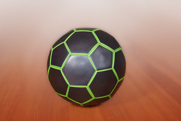 The black and green ball for football or volleyball playing, in the center of composition. Indoors, selective focus, blur background. Sport or fintess concept, copy space.