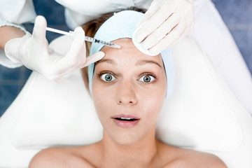 Beautiful girl at the reception of a dermatologist in the health clinic. Dermatologist conducting the procedure on the skin of the face makes an injection into the wrinkles on the forehead