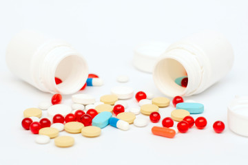 Multicolored natural tablets and vitamins poured out of the jar on a white background.