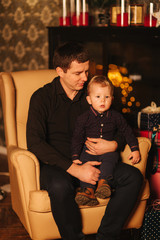 Handsome man with son sitting on the armchair at home. Christmas mood