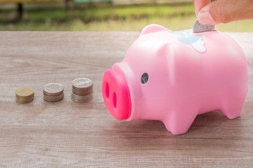 The hand picking coin-operated, put a pink piggy bank with a coin pile on the side, on wooden floor.