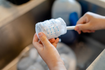 Mother hand washing baby milk bottle with brush