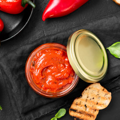 Grilled red pepper sauce (lutenica)  in glass jar with toasted bread.