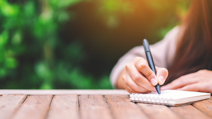 Closeup image of a woman writing on blank notebook on wooden table in the outdoors - obrazy, fototapety, plakaty