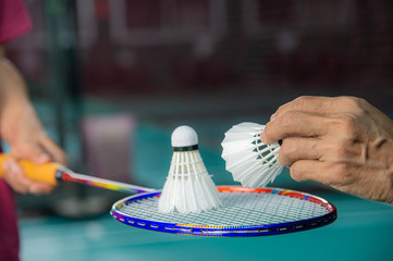Badminton player holding racket with used Badminton shuttlecock on top and hand of service judge hold new shuttlecock to change the new one with blur background.