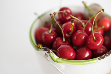 Ripe red cherry in a white garden enamel bucket with a green border on a white background close-up
