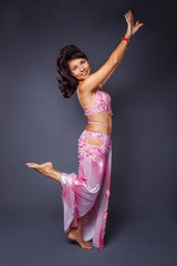 Belly dancer performing belly dance in the ethnic pink costume for dancing on gray background