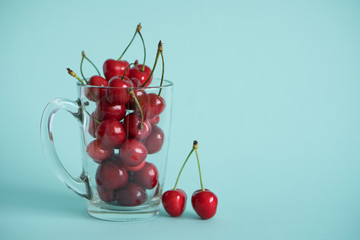 ripe cherries in a glass transparent mug on a bright contrasting blue turquoise background next to a eyelid with berries