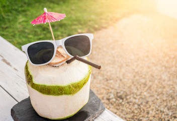 Fresh coconut juice wearing sunglasses on wood white table in sunlight