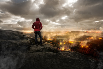 Mann steht auf einen Berg und schaut auf eine brennende Landschaft