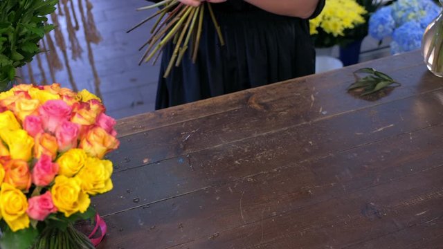 Floral business concept. Florist woman works makes bouquet of brown maroon color peonies in flower shop, hands closeup. She creates professional bunch composition in floristic studio store on table.